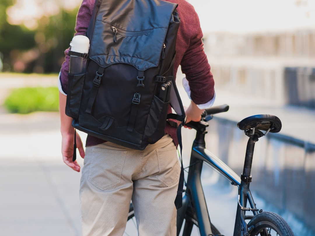 Symbolbild: männliche Person mit Rucksack von hinten, die ein Rad schiebt.